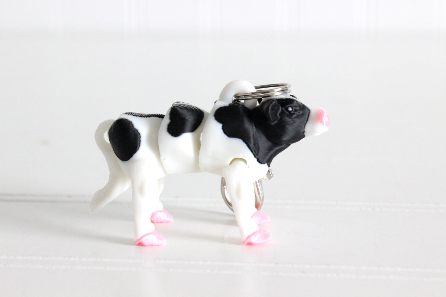 3D-printed black-and-white cow keychain with a silver swivel quick-clip on a white background.