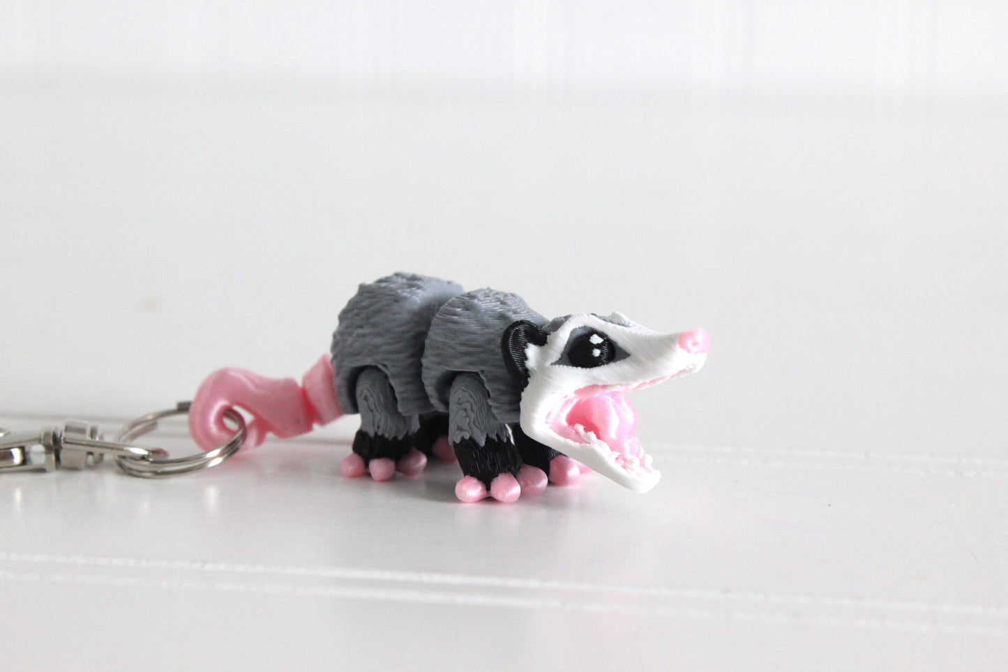 3D-printed gray-and-white opossum keychain with a silver swivel quick-clip on a white background.