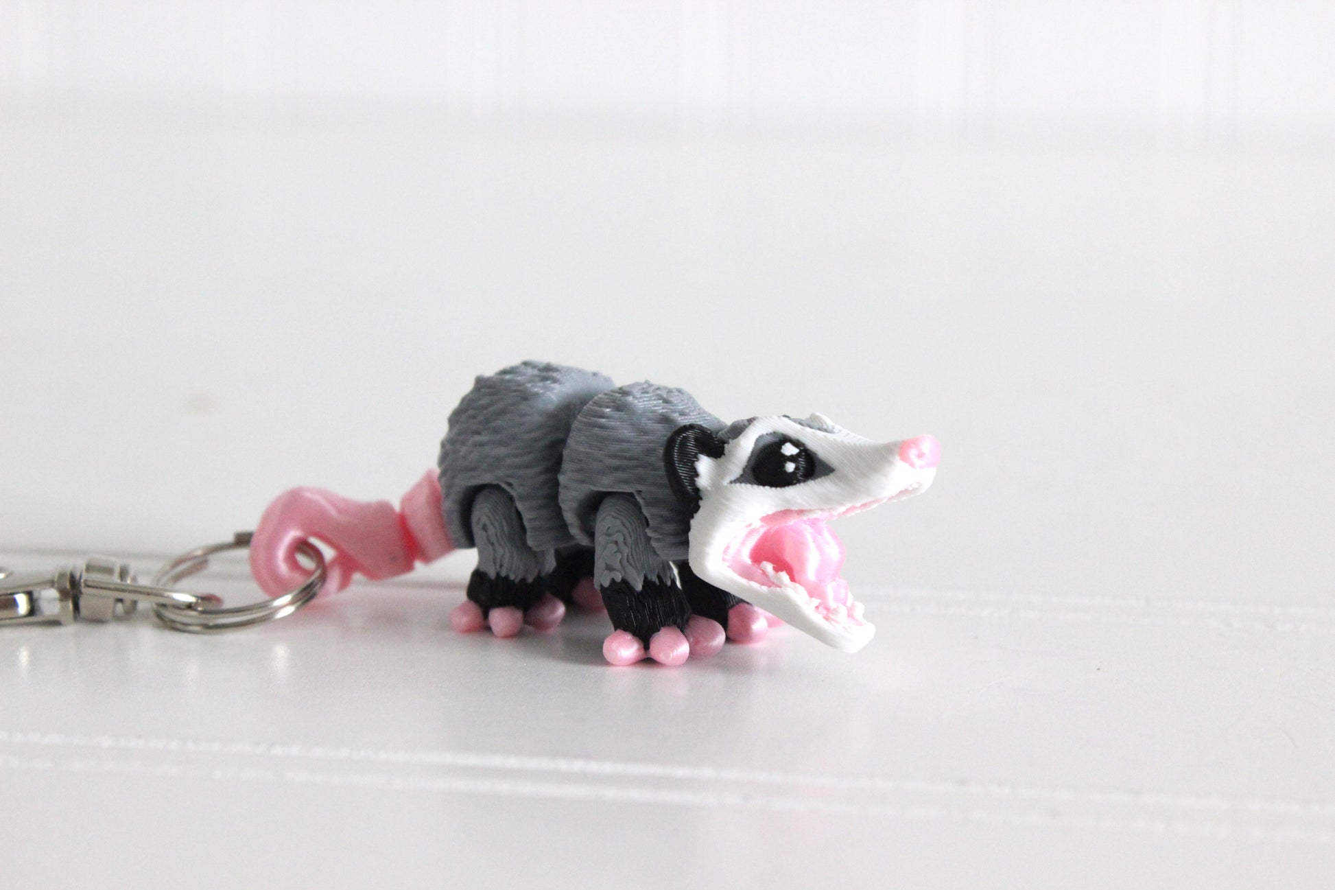 3D-printed gray-and-white opossum keychain with a silver swivel quick-clip on a white background.