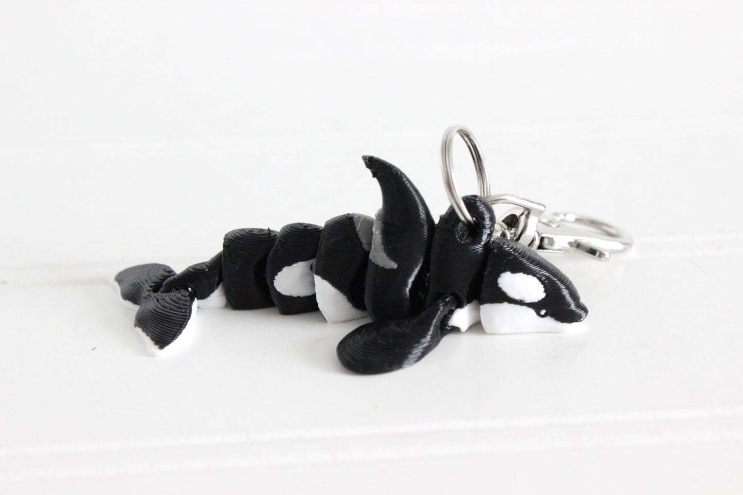 3D-printed black-and-white orca keychain with a silver swivel quick-clip on a white background.