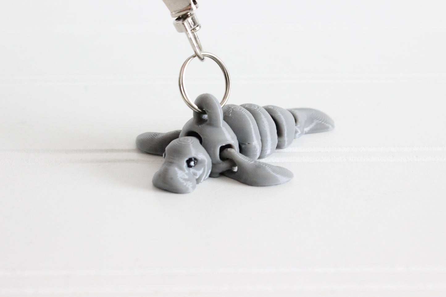 3D-printed gray manatee keychain with a silver swivel quick-clip on a white background.
