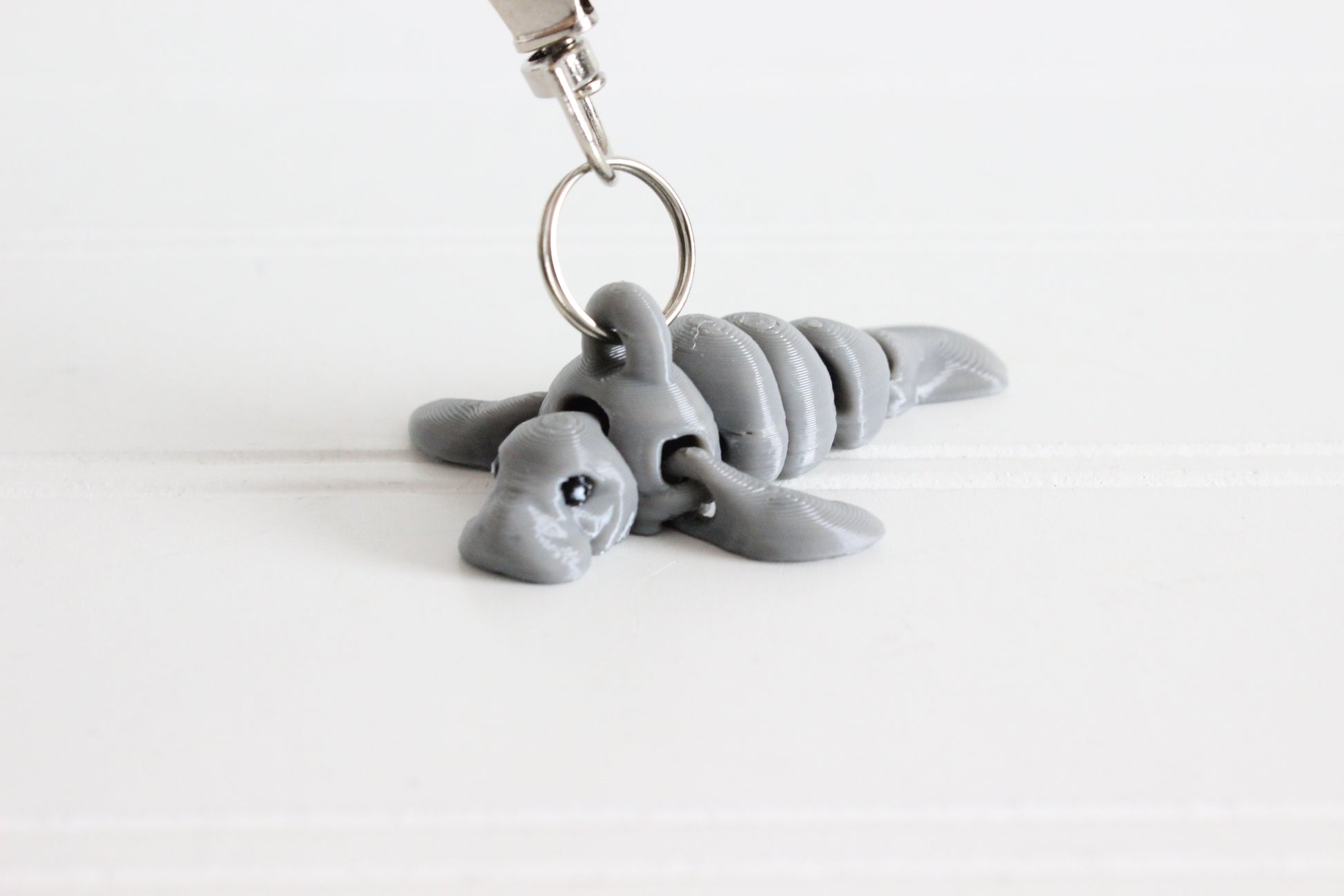 3D-printed gray manatee keychain with a silver swivel quick-clip on a white background.