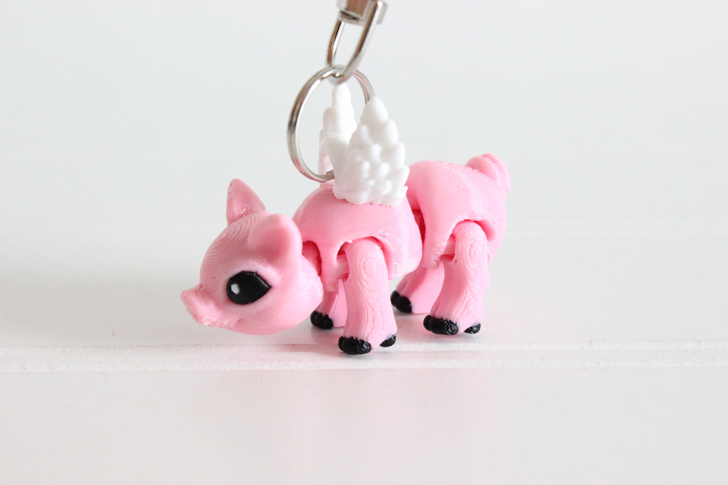 3D-printed pink winged pig keychain with a silver swivel quick-clip on a white background.