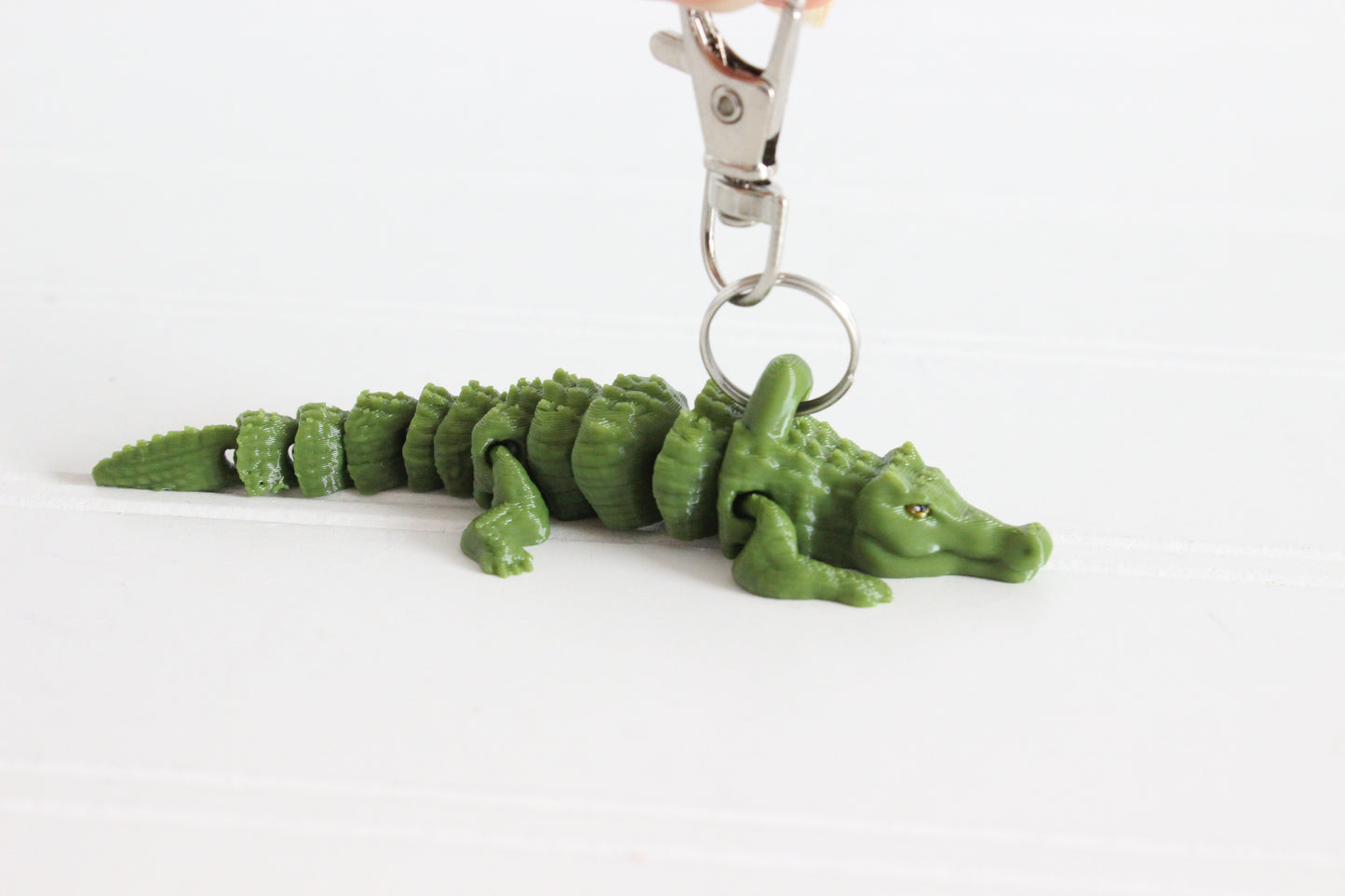 Side view of a green 3D-printed alligator keychain resting on a white surface.