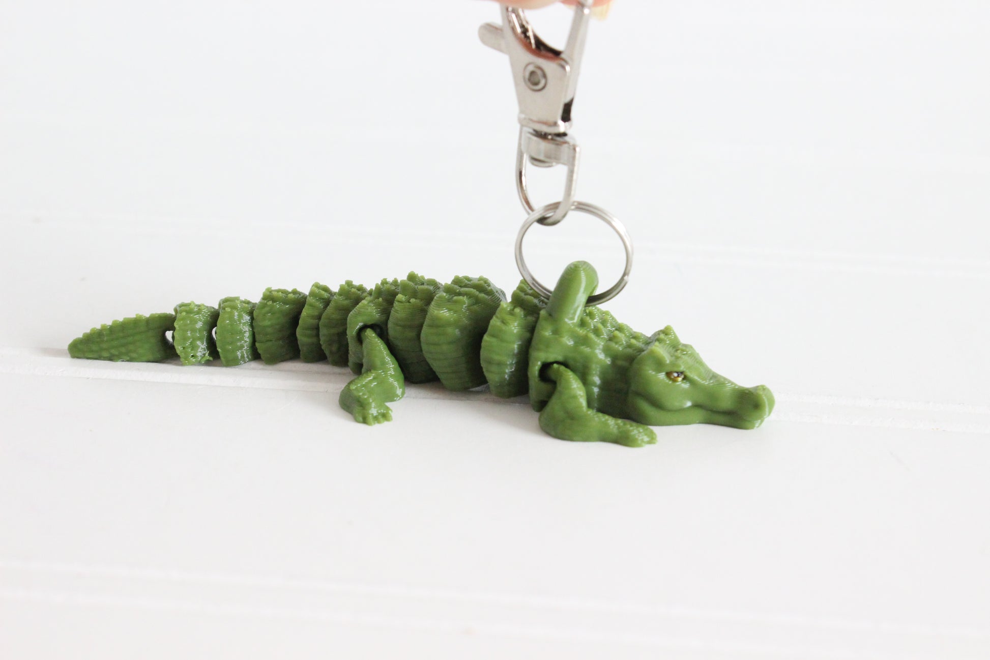 Side view of a green 3D-printed alligator keychain resting on a white surface.