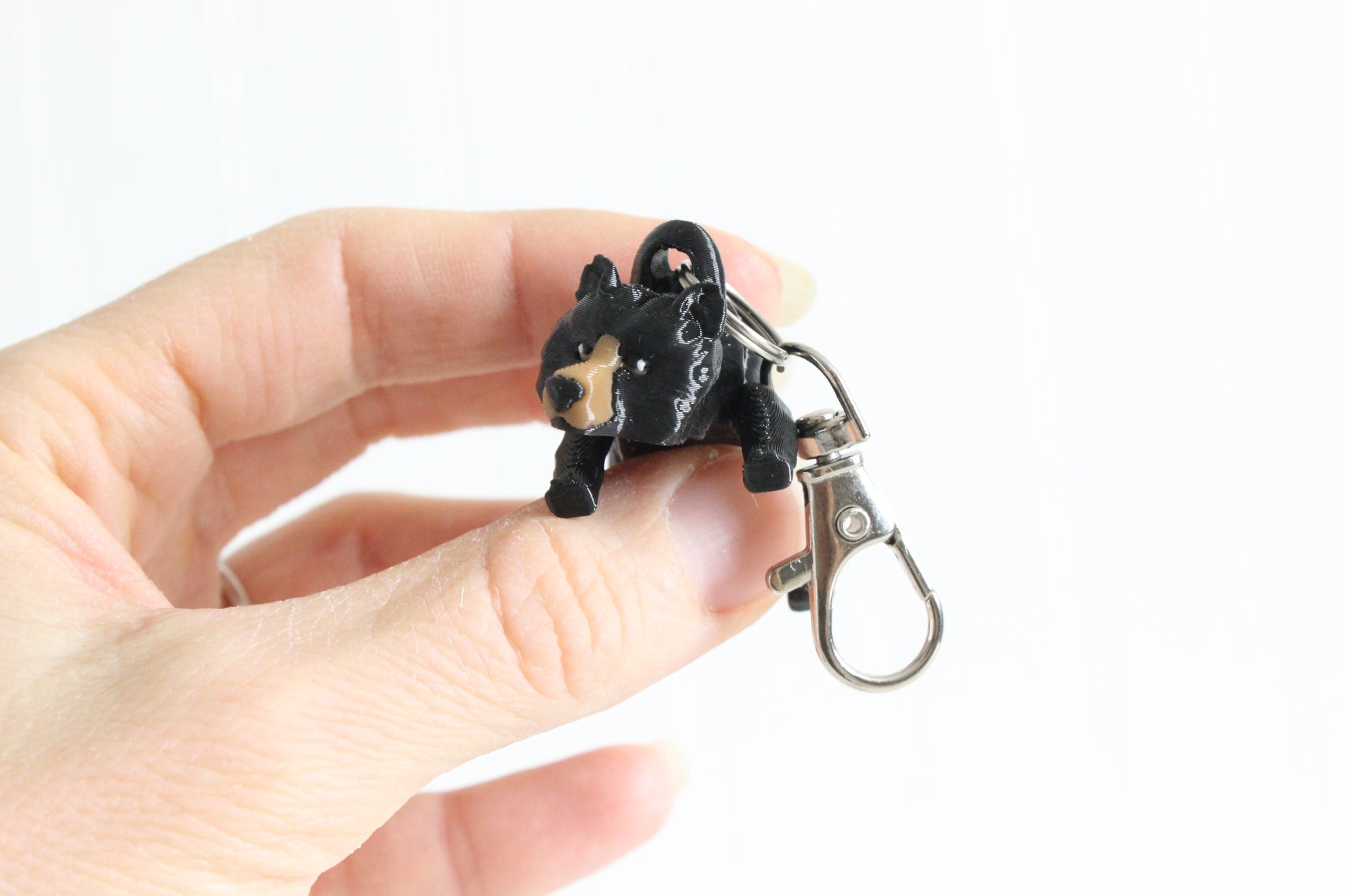 Hand holding 3D-printed black bear keychain to show its size, colors, and silver swivel clip.