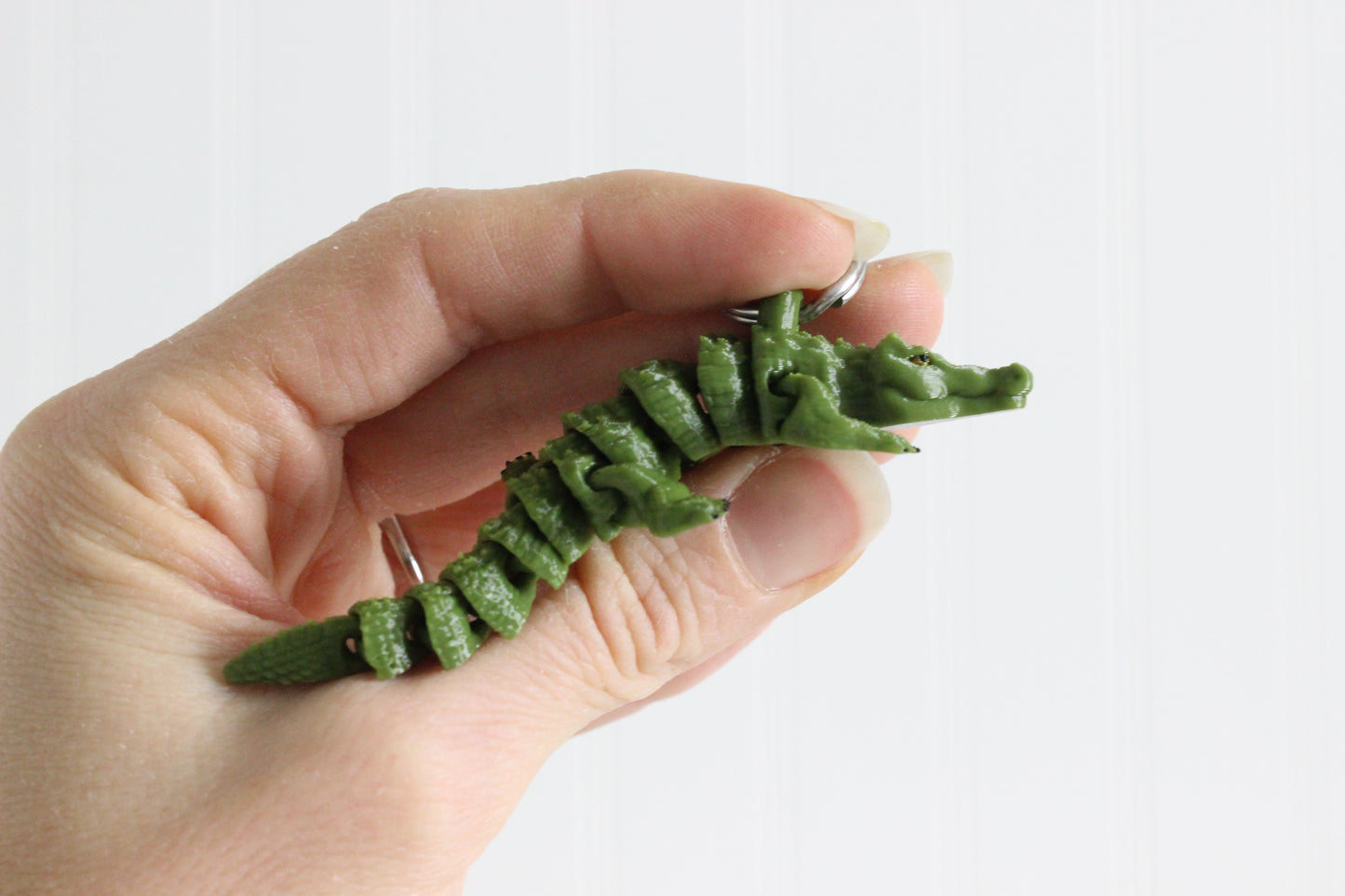 Side view of a green 3D-printed alligator keychain held in a person's hand.