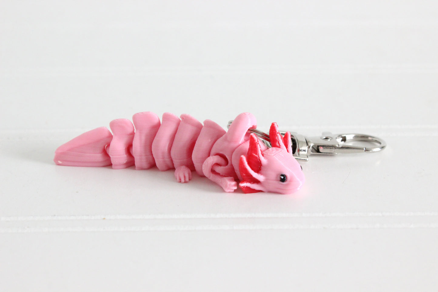 Side view of a pink 3D-printed axolotl keychain on a white background.