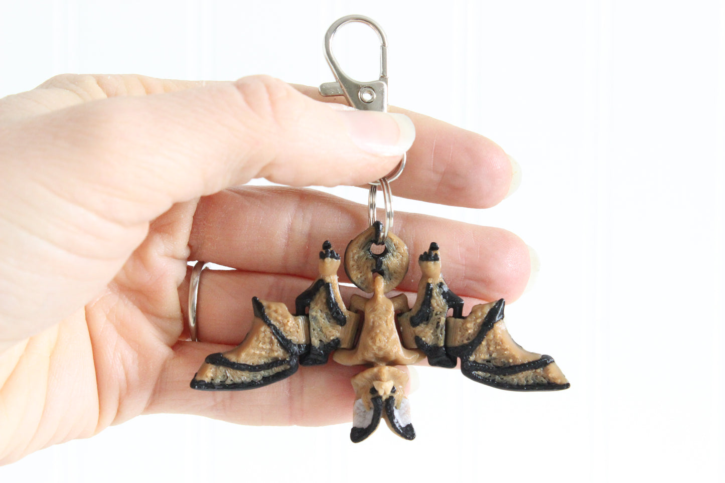Hand holding a 3D-printed bat keychain to show its size and wing shape.
