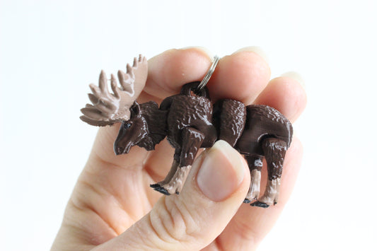 Hand holding 3D-printed brown moose with antlers keychain to show its size, colors, and silver swivel clip.