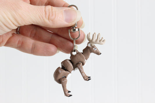 Hand holding the 3D-printed brown buck with antlers keychain to show its size, colors, and silver swivel clip.