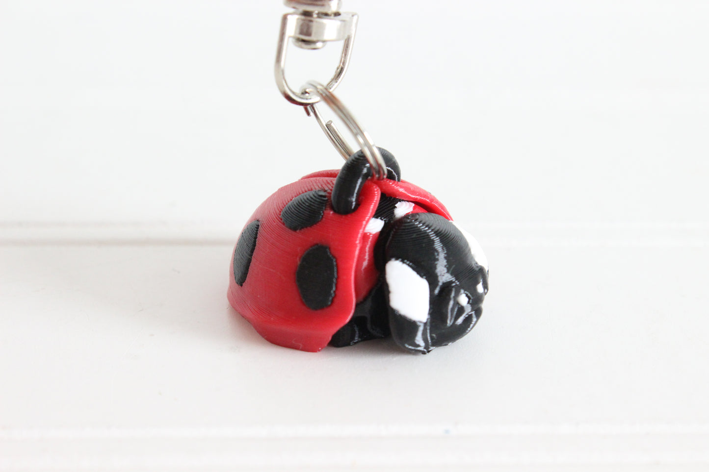 3D-printed red-and-black ladybug keychain with a silver swivel quick-clip on a white background.