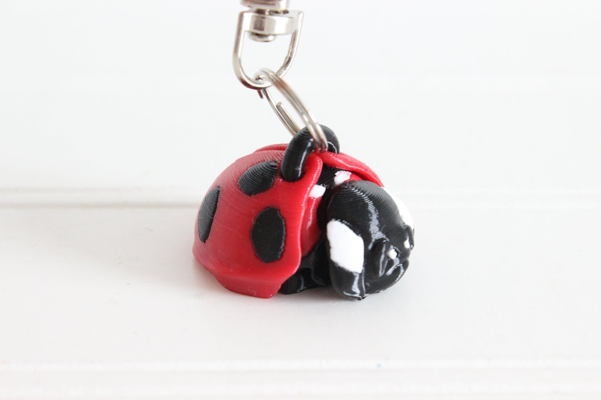 3D-printed red-and-black ladybug keychain with a silver swivel quick-clip on a white background.