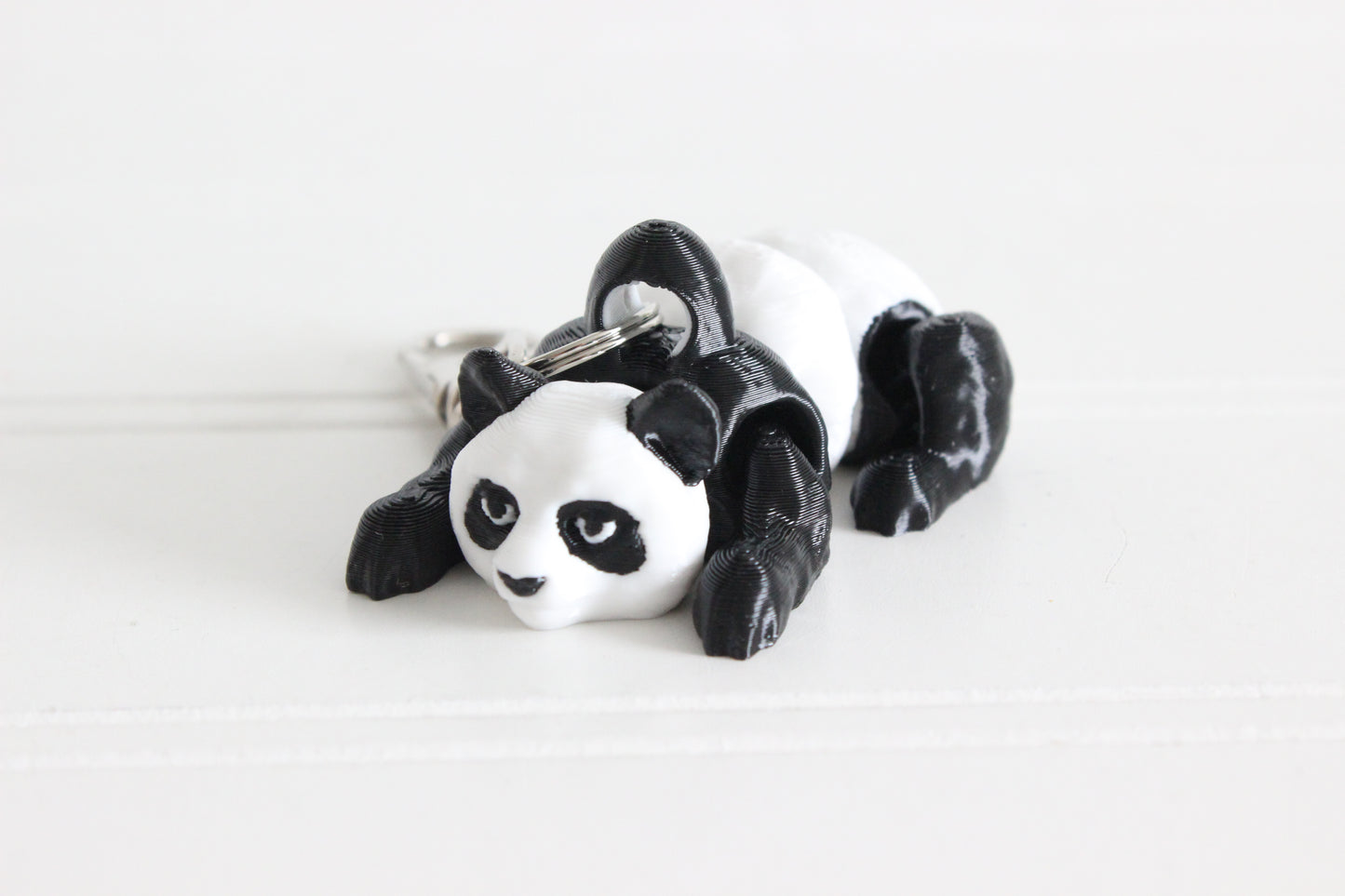 Hand holding the 3D-printed black-and-white panda bear keychain to show its size, colors, and silver swivel clip.