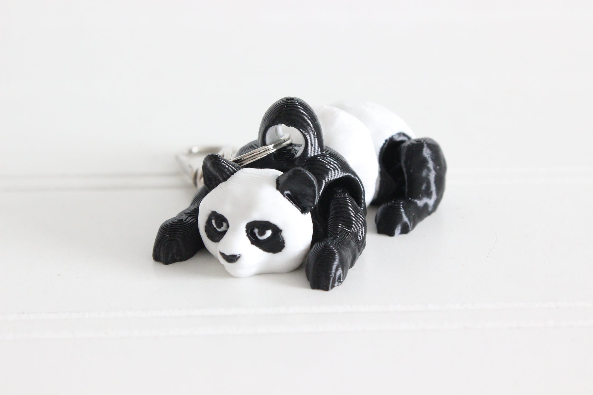 Hand holding the 3D-printed black-and-white panda bear keychain to show its size, colors, and silver swivel clip.