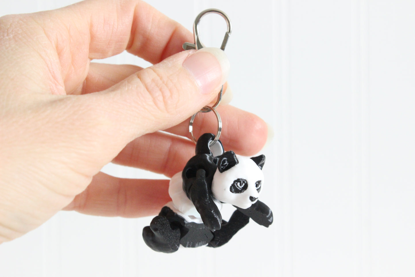 Hand holding the 3D-printed black-and-white panda bear keychain to show its size, colors, and silver swivel clip.