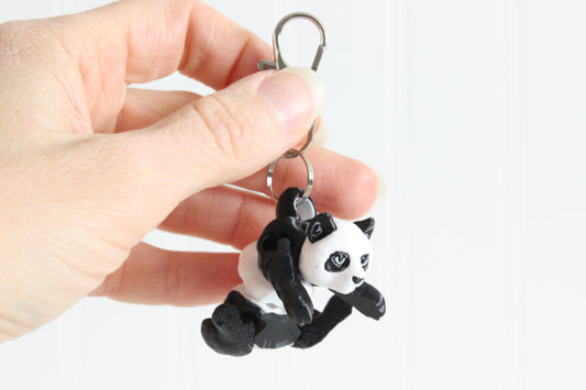 Hand holding the 3D-printed black-and-white panda bear keychain to show its size, colors, and silver swivel clip.