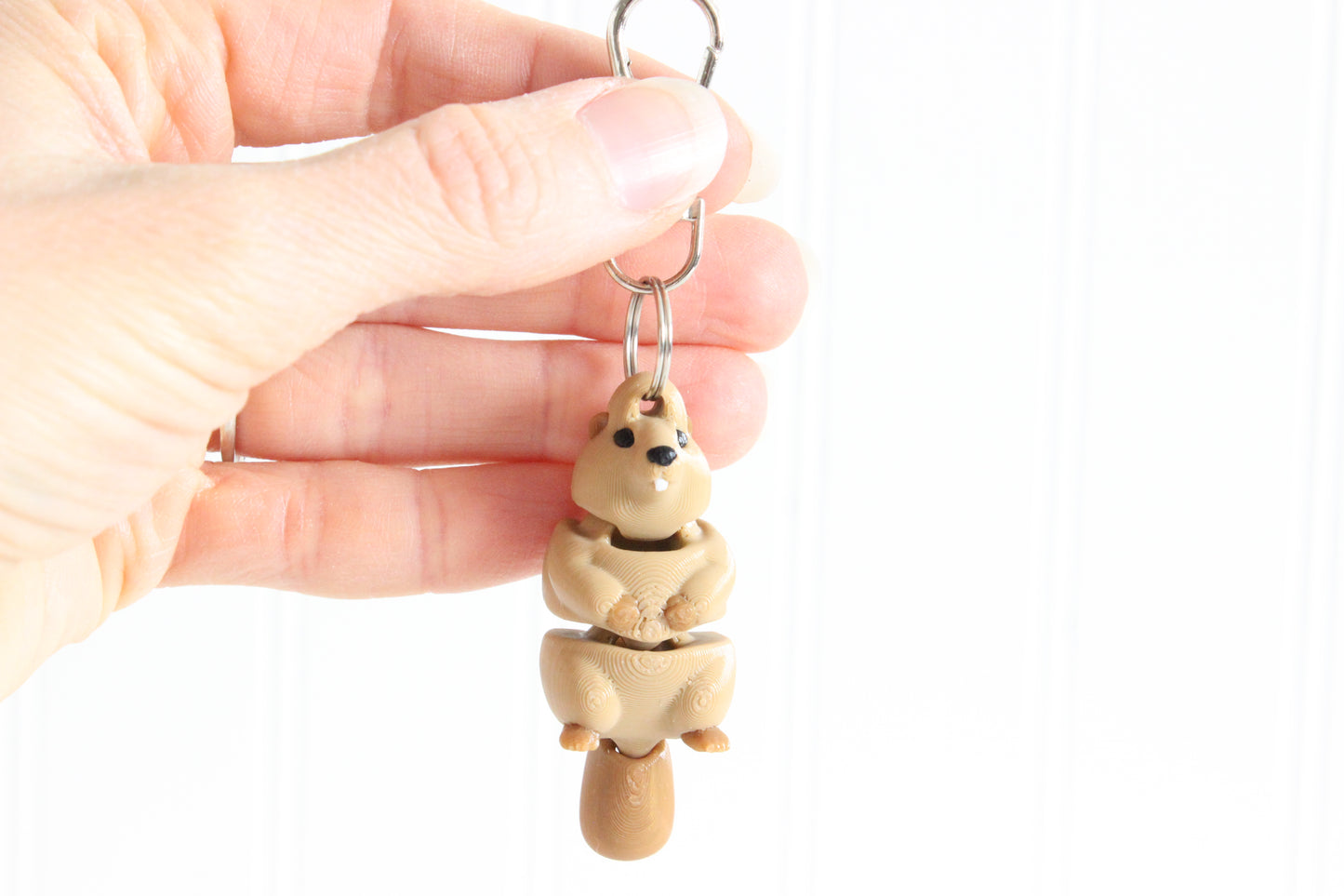 Hand holding the 3D-printed brown beaver keychain to show its size, colors, and silver swivel clip.