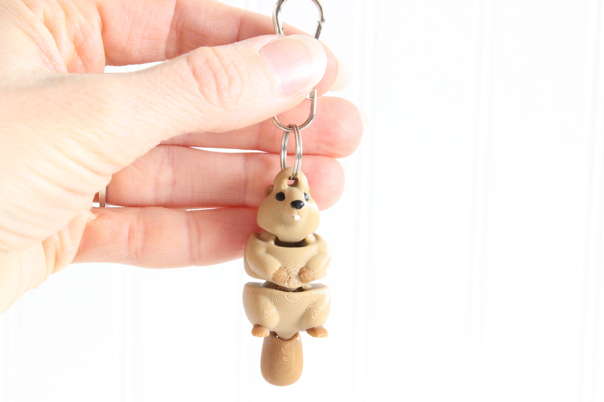 Hand holding the 3D-printed brown beaver keychain to show its size, colors, and silver swivel clip.