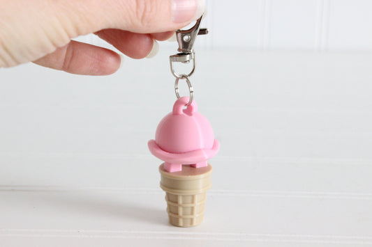 Hand holding 3D-printed strawberry ice cream cone keychain to show its size, colors, and silver swivel clip.