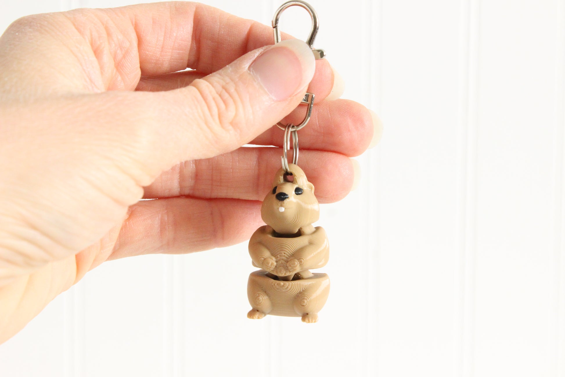Hand holding the 3D-printed brown groundhog keychain to show its size, colors, and silver swivel clip.