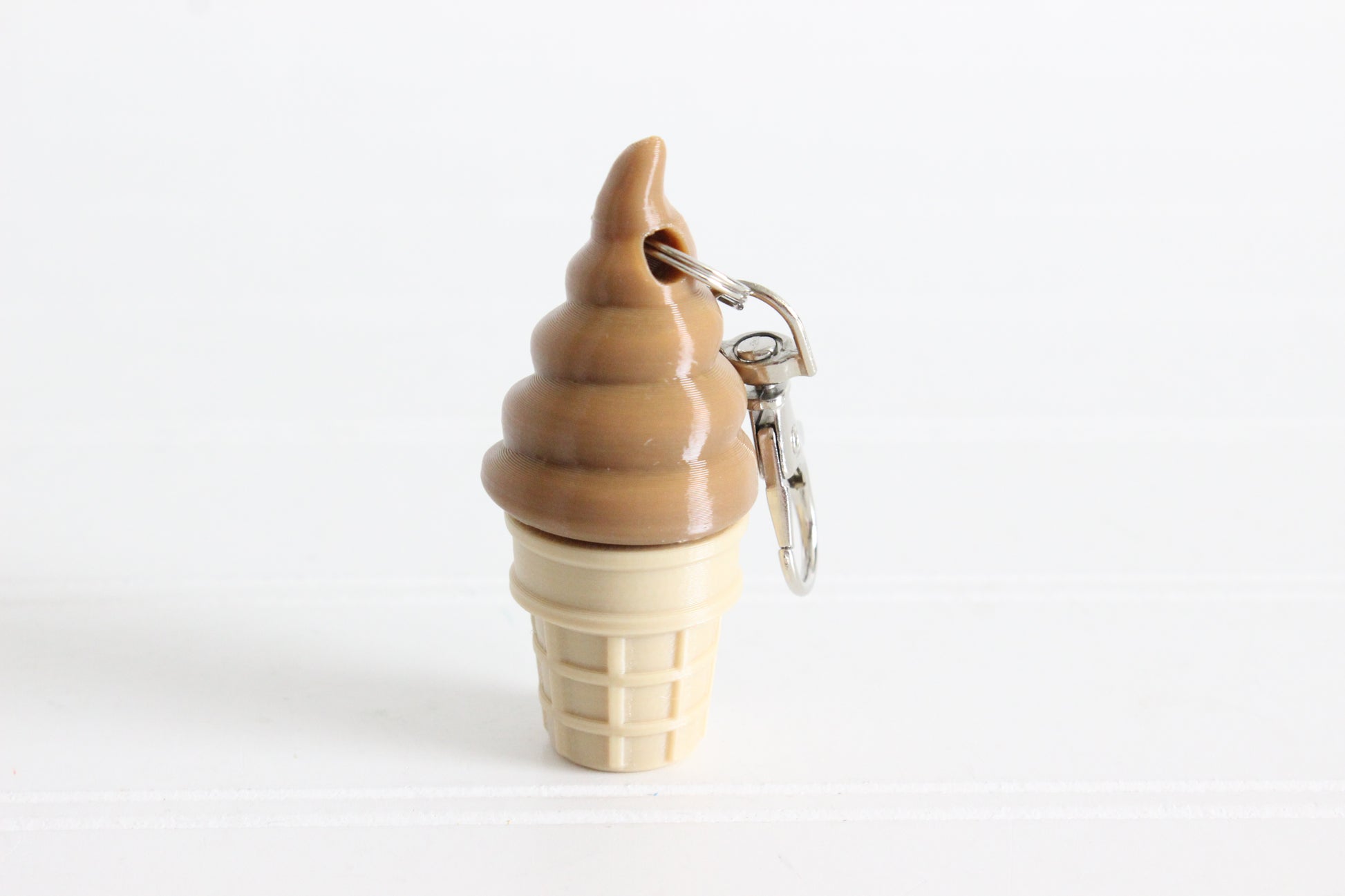 3D-printed chocolate soft-serve ice cream cone keychain with a metal key ring on a white background.