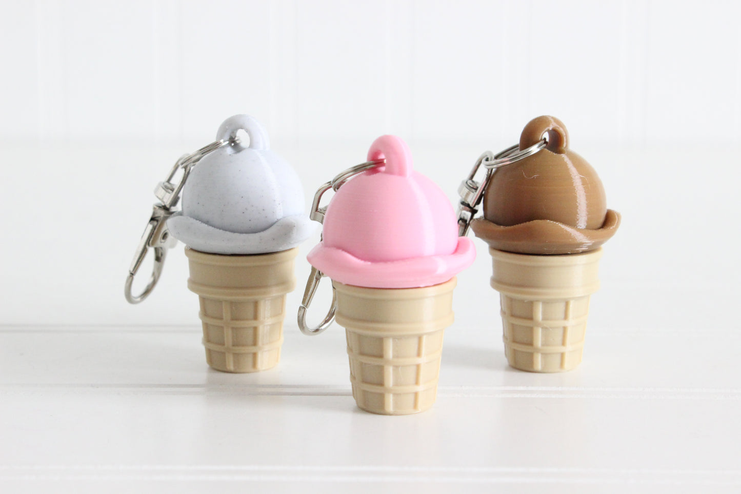 Cookies-and-cream, strawberry, and chocolate scoop ice cream cone keychains displayed together.