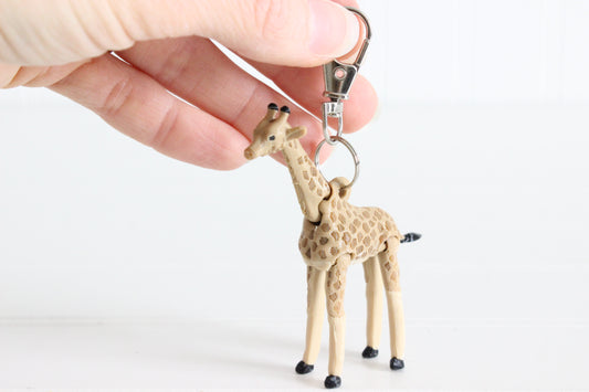 Hand holding 3D-printed tan giraffe with brown spots keychain to show its size, colors, and silver swivel clip.
