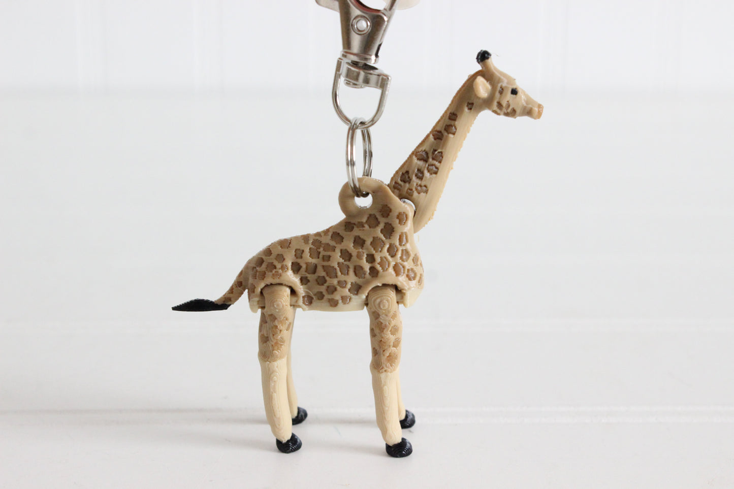 3D-printed tan giraffe with brown spots keychain with a silver swivel quick-clip on a white background.