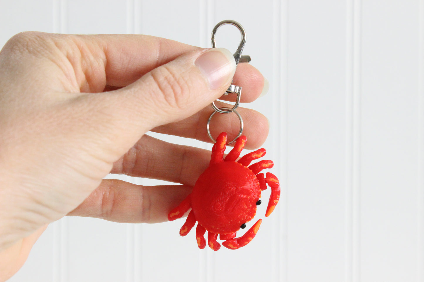 Hand holding the 3D-printed red crab keychain to show its size, colors, and silver swivel clip.