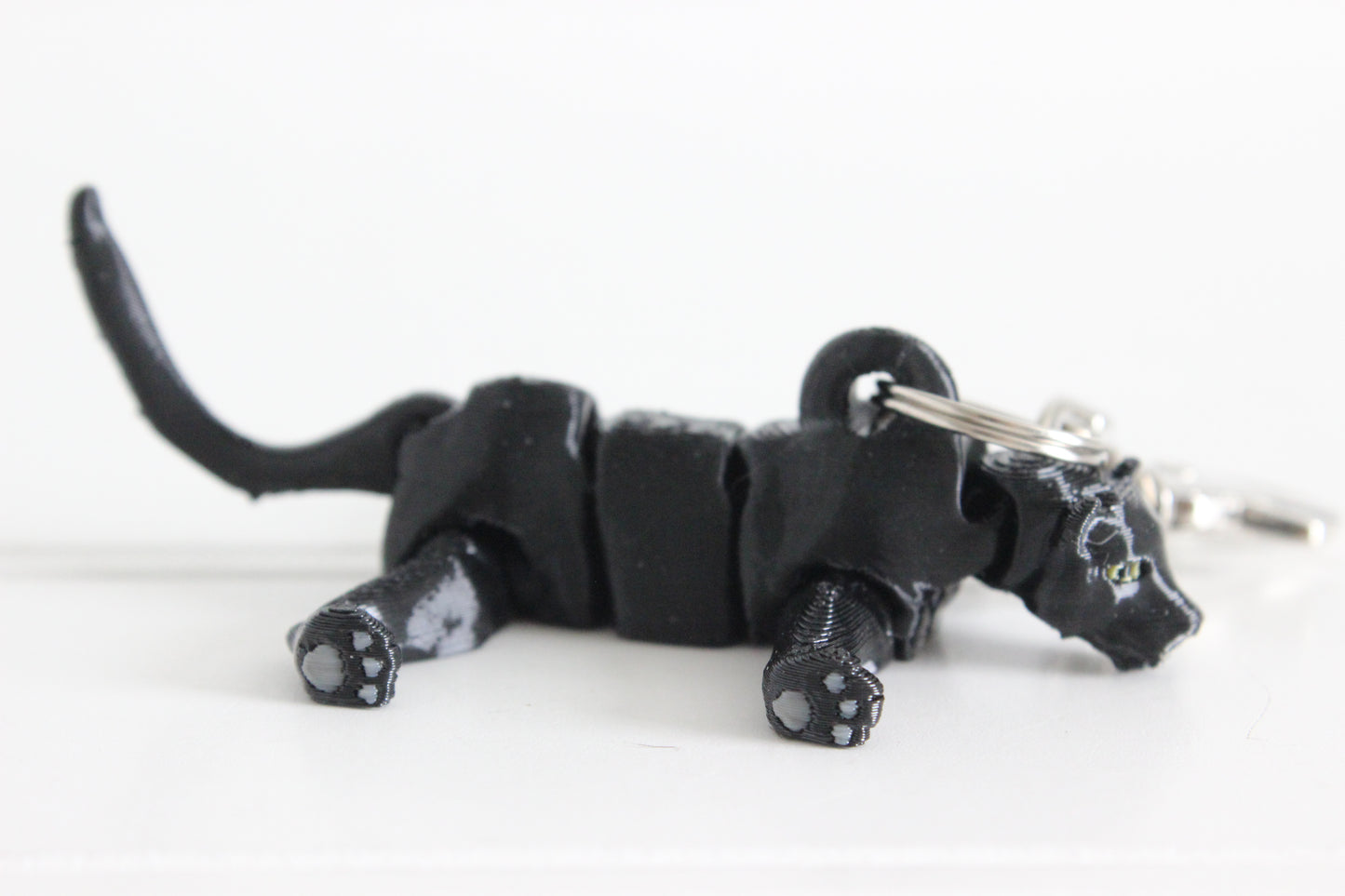 Side view of the articulated black panther keychain lying down, showing flexible joints, raised tail, and detailed paw pads.