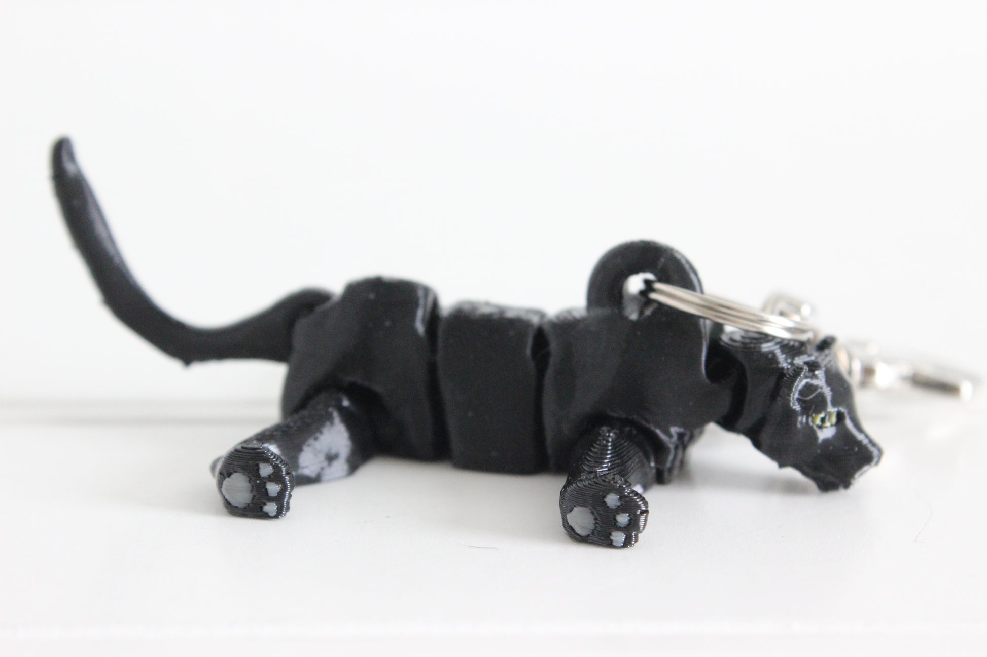 Side view of the articulated black panther keychain lying down, showing flexible joints, raised tail, and detailed paw pads.