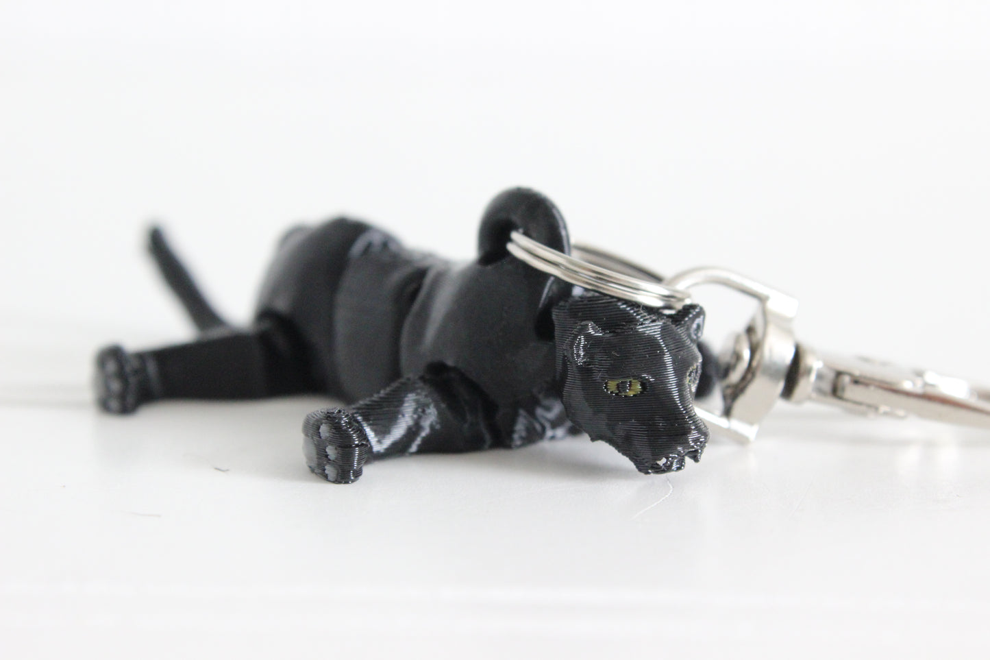 Articulated black panther keychain lying down with sculpted facial features and silver swivel quick-clip.