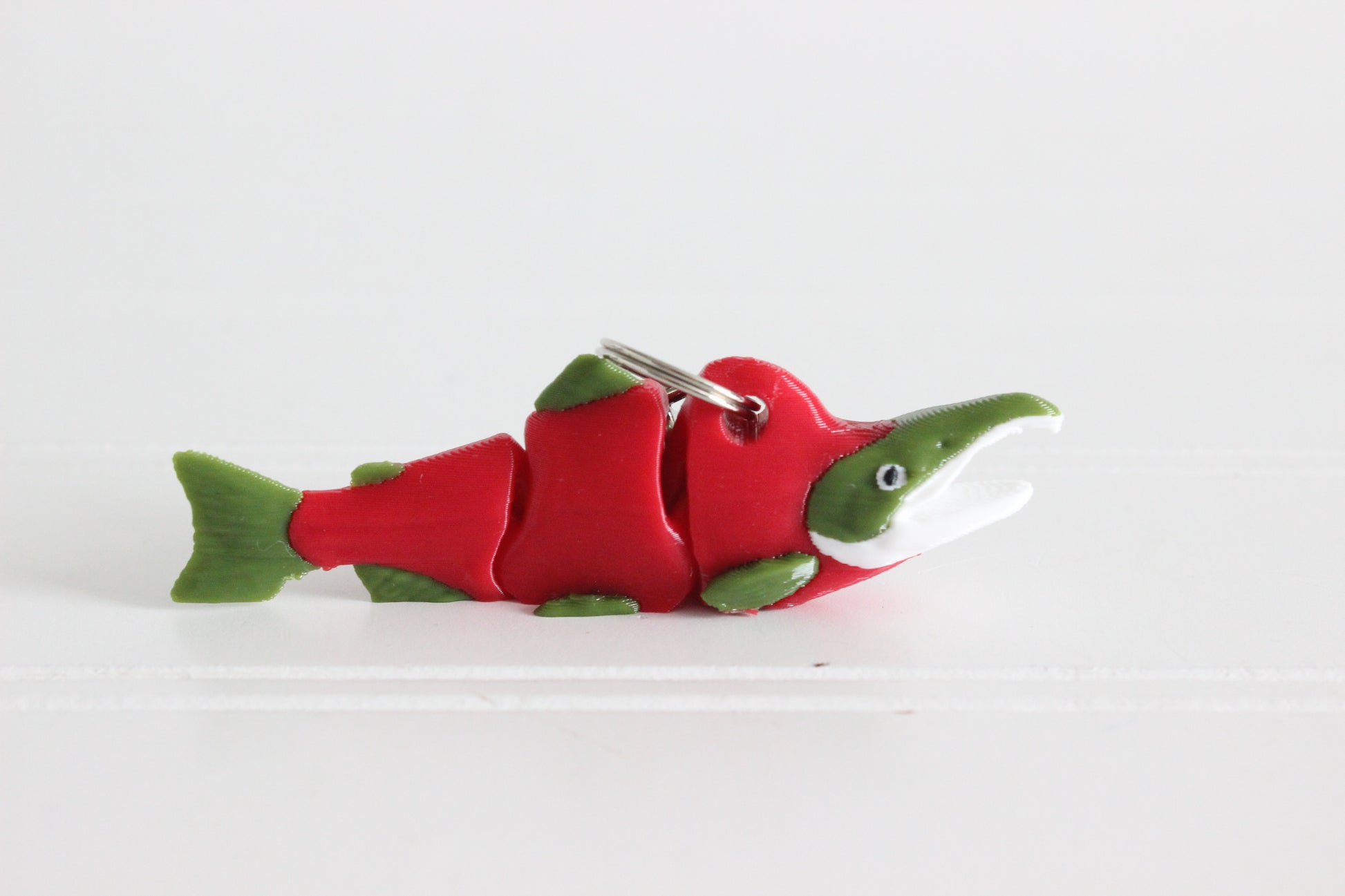 3D printed sockeye salmon keychain with red body and green fins, lying flat on a white background with metal key ring