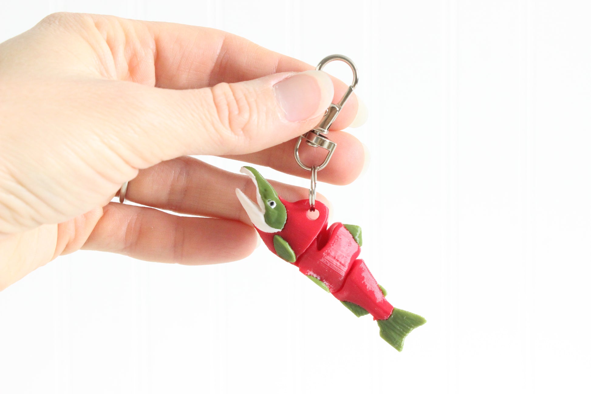 Hand holding a 3D printed sockeye salmon keychain with swivel quick-clip key ring, showing red body and green fin detail