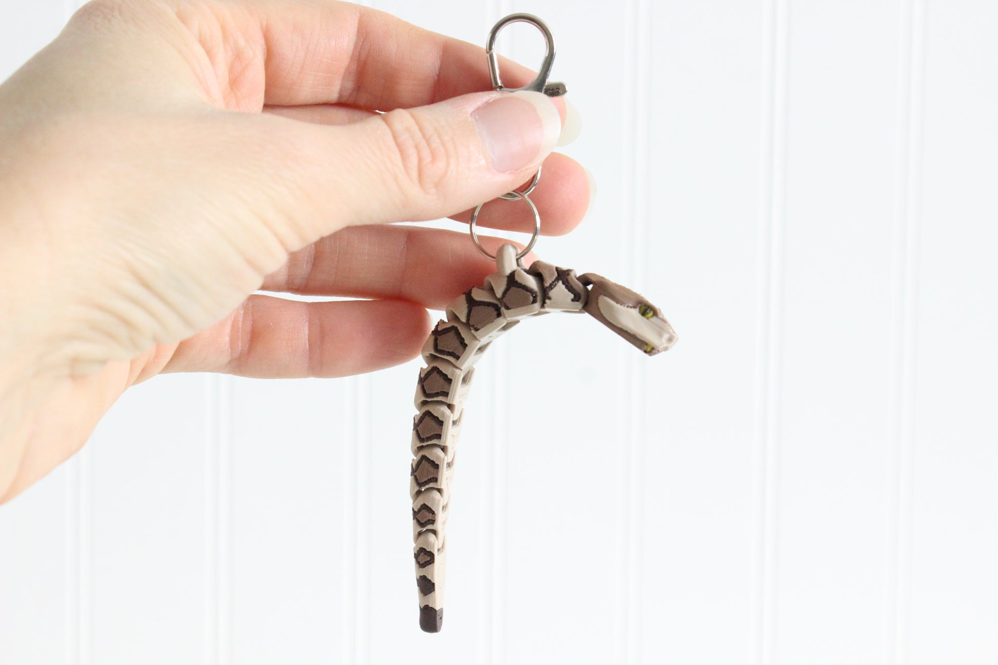 Hand holding the articulated copperhead snake keychain for size reference.