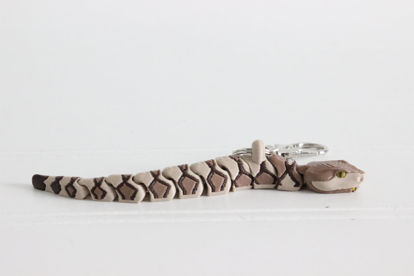 Side view of an articulated copperhead snake keychain with tan and brown banded pattern.
