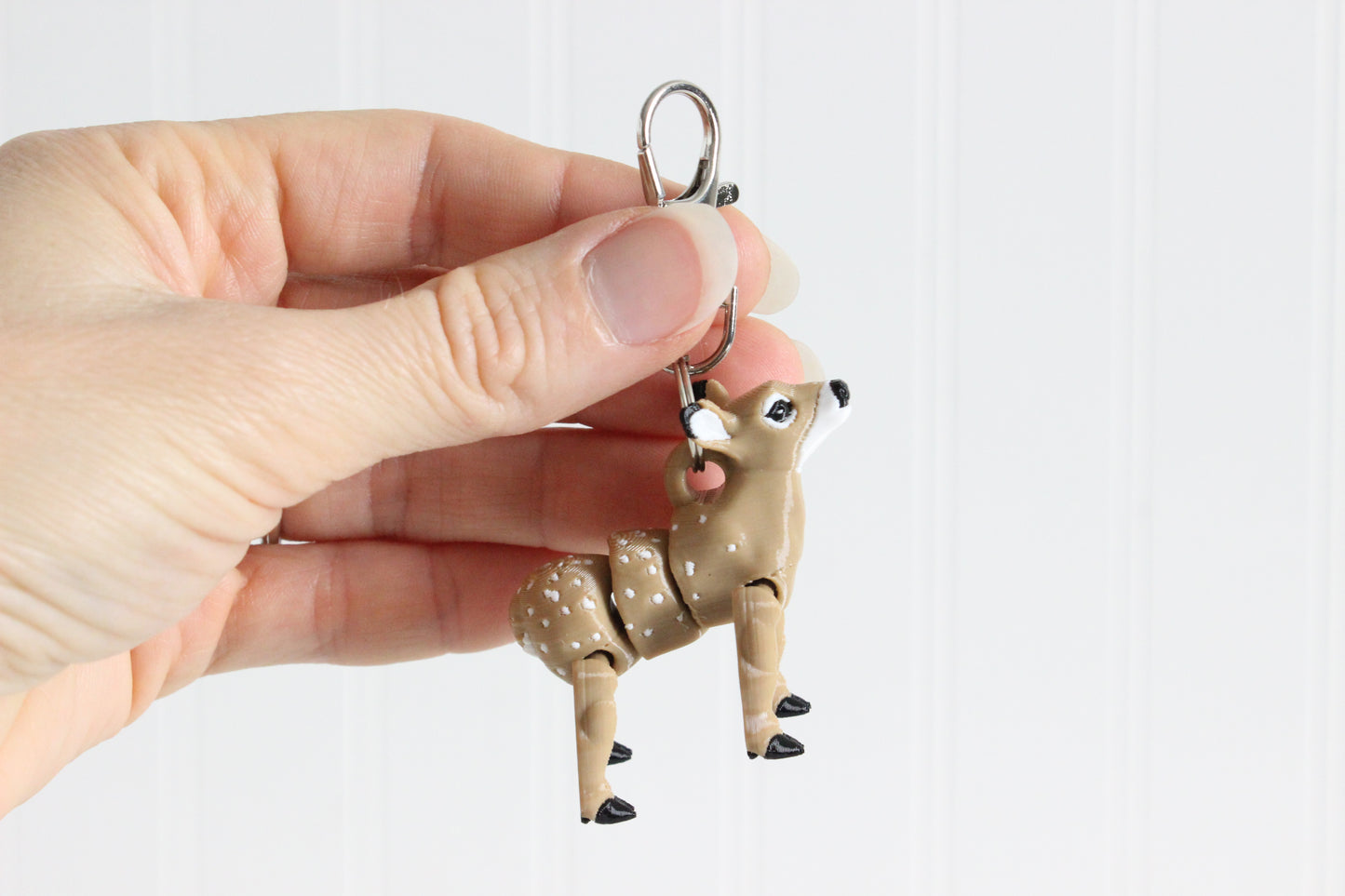 Hand holding the 3D-printed brown doe keychain to show its size, colors, and silver swivel clip.