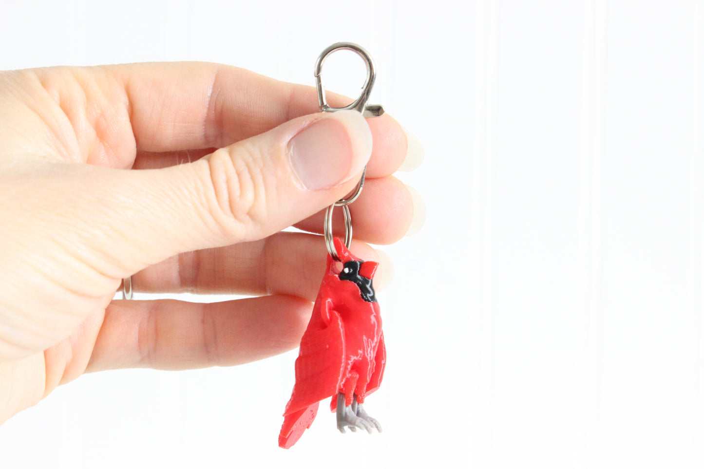 Hand holding the 3D-printed red cardinal keychain to show its size, colors, and silver swivel clip.