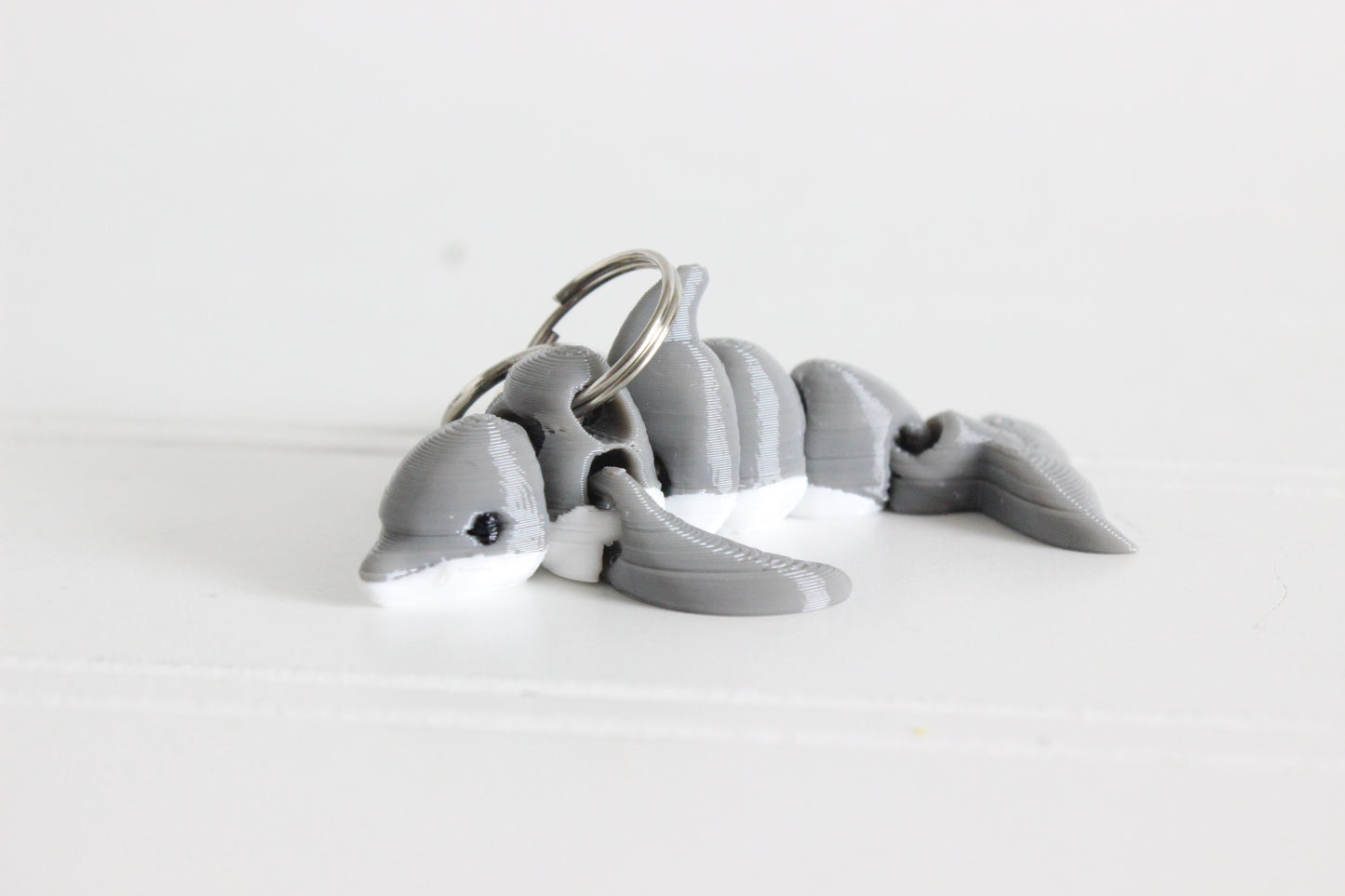3D-printed gray dolphin keychain with a silver swivel quick-clip on a white background.