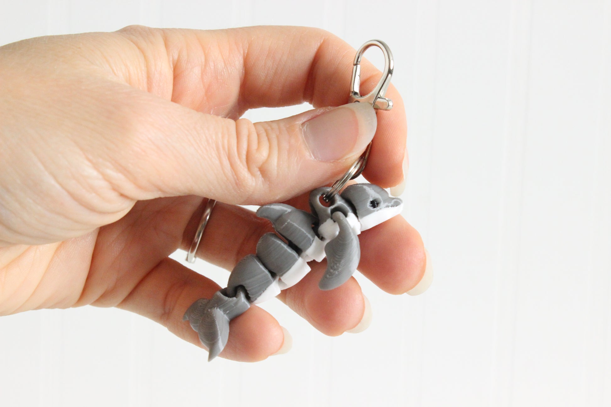 Hand holding the 3D-printed gray dolphin keychain to show its size, colors, and silver swivel clip.