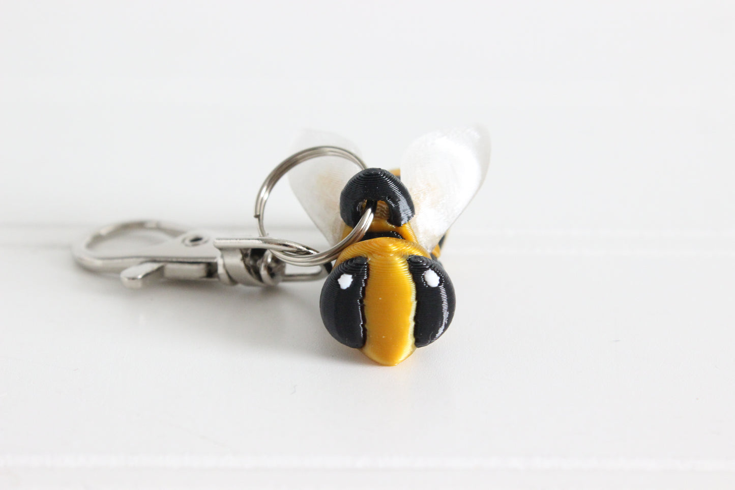 Close-up of the 3D-printed yellow-and-black bee with translucent wings keychain showing its face, markings, and textured surface.