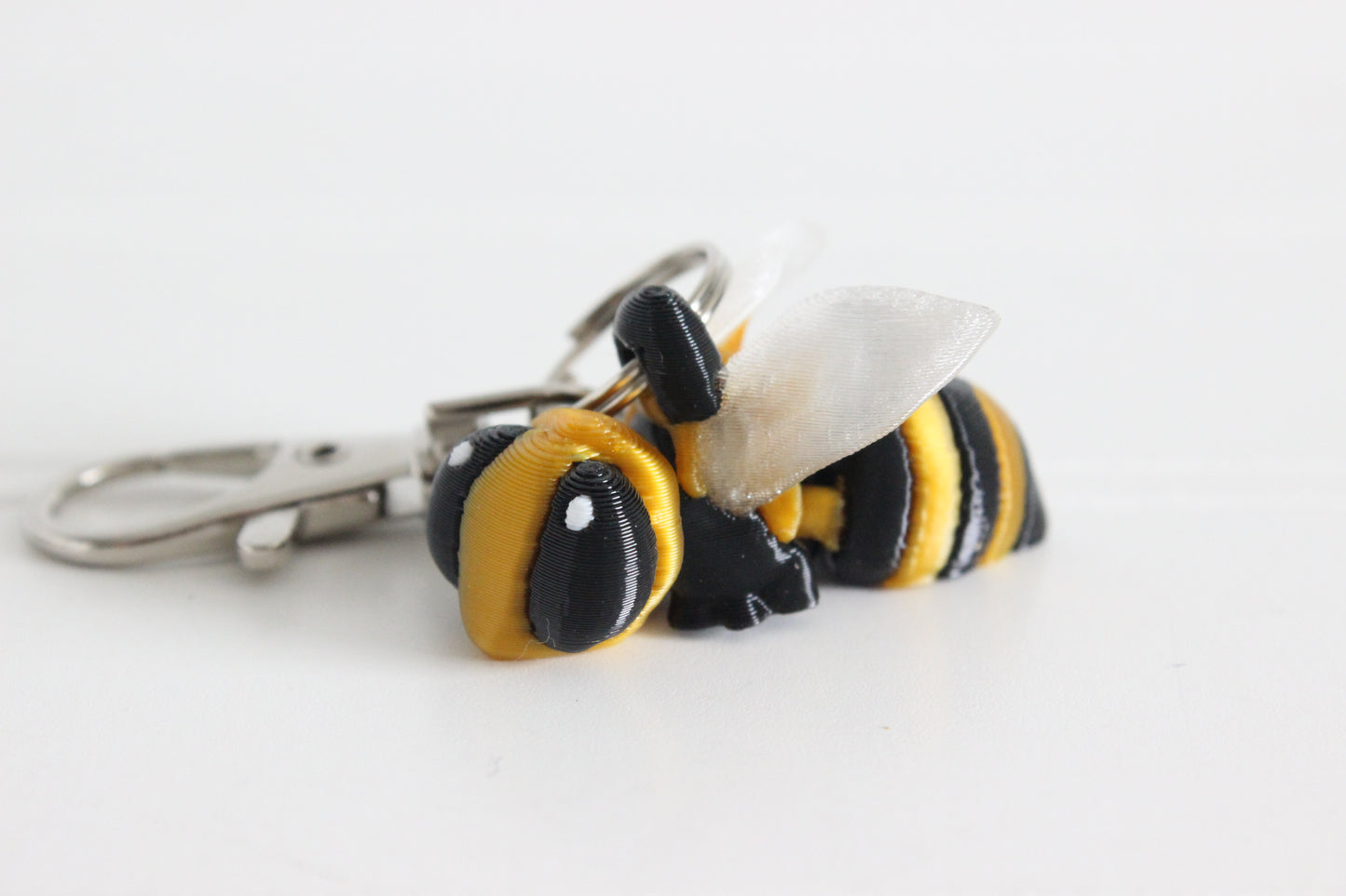 3D-printed yellow-and-black bee with translucent wings keychain with a silver swivel quick-clip on a white background.