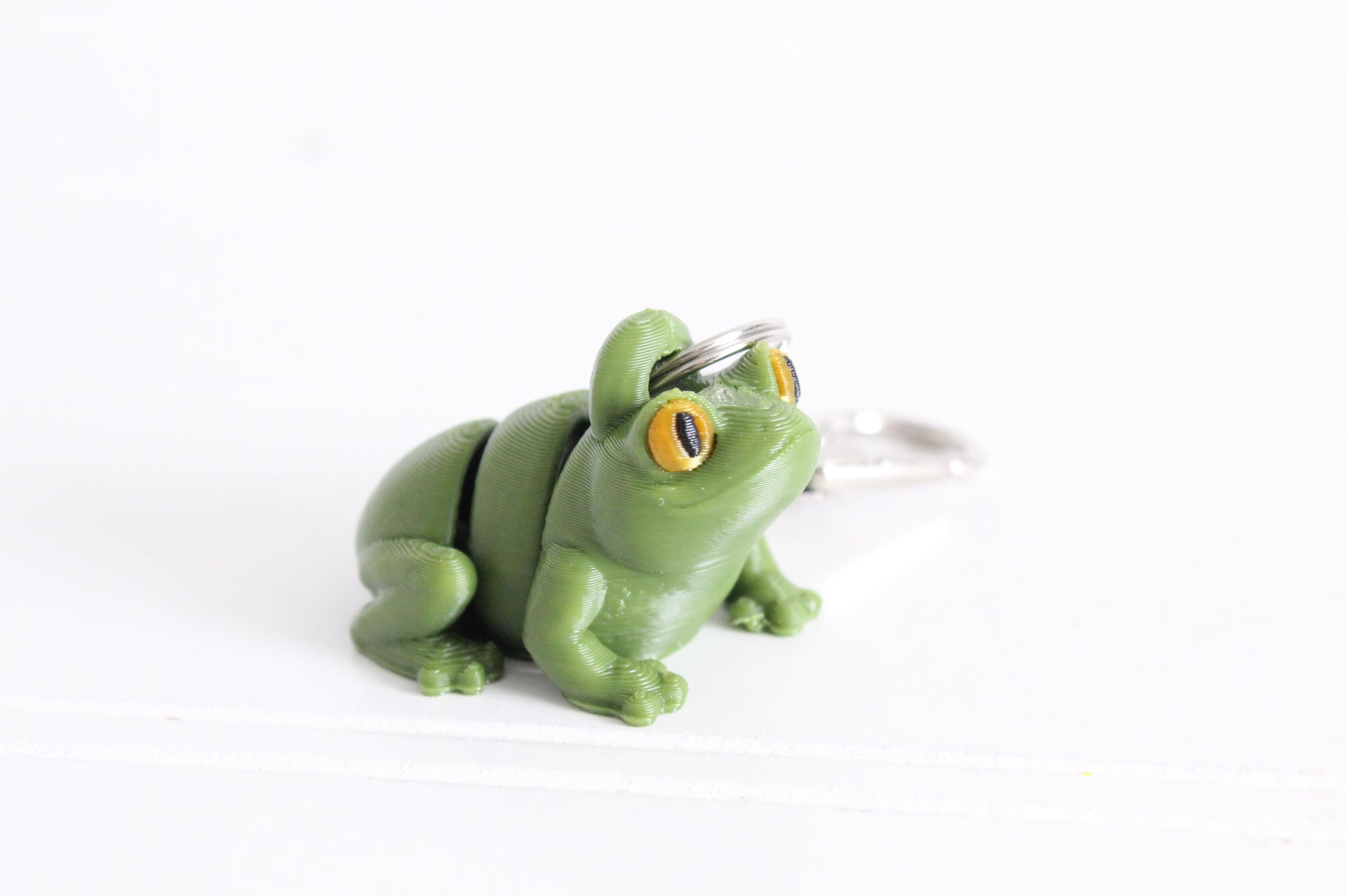3D-printed green frog keychain with a silver swivel quick-clip on a white background.