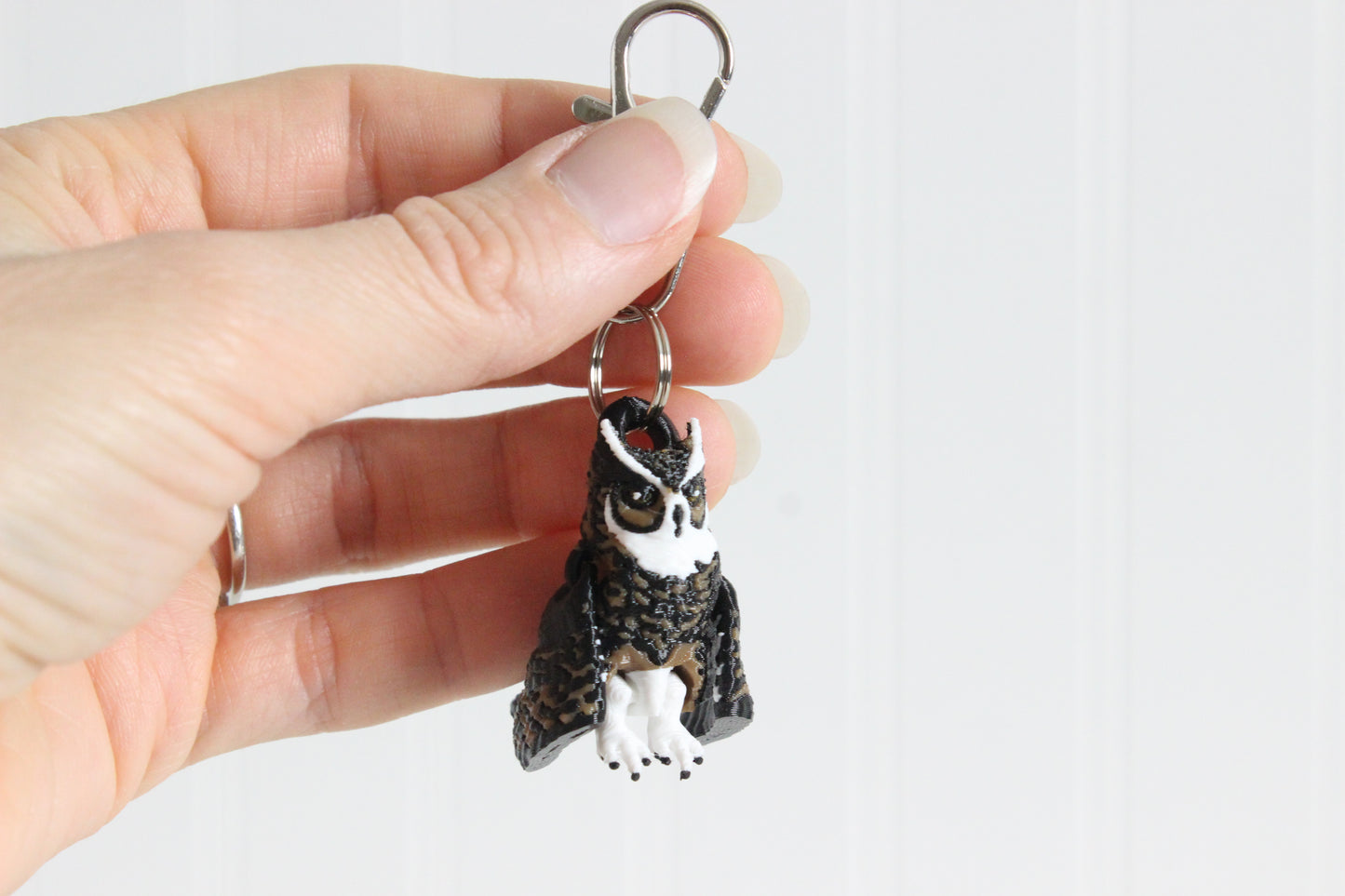 Hand holding 3D-printed brown great horned owl keychain to show its size, colors, and silver swivel clip.