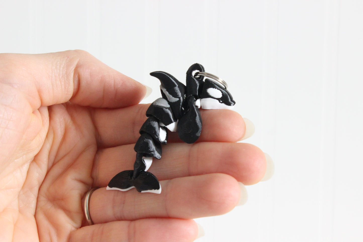 Hand holding the 3D-printed black-and-white orca keychain to show its size, colors, and silver swivel clip.