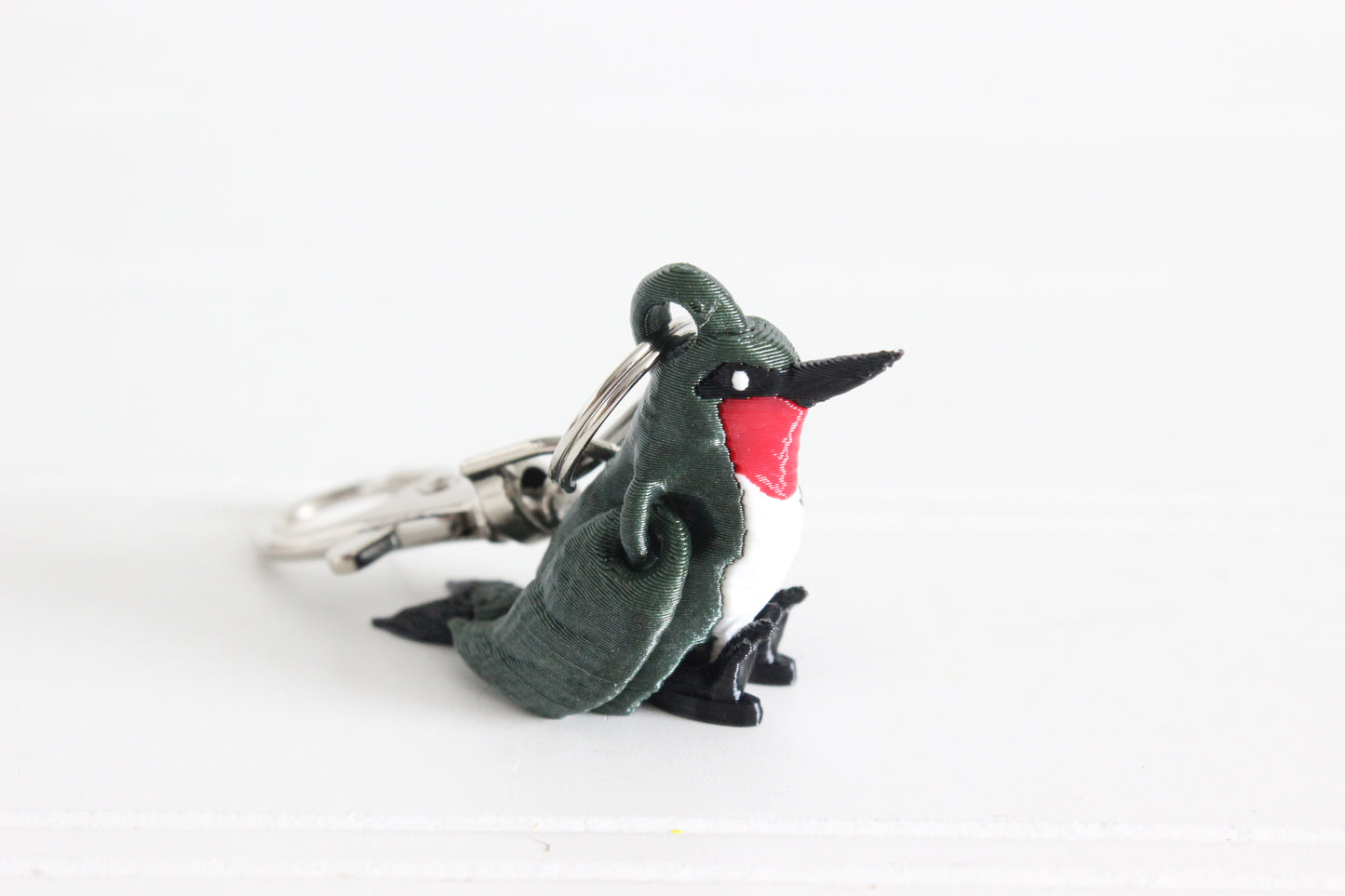 3D-printed green hummingbird keychain with a silver swivel quick-clip on a white background.