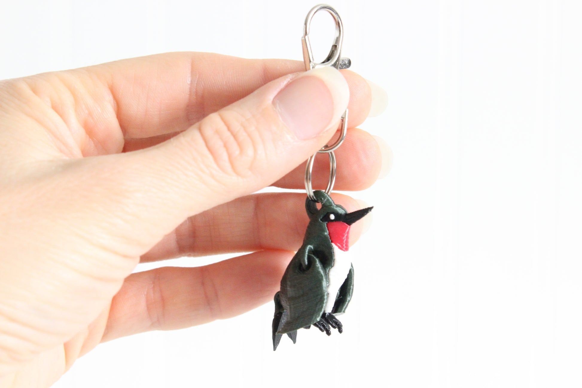 Hand holding 3D-printed green hummingbird keychain to show its size, colors, and silver swivel clip.
