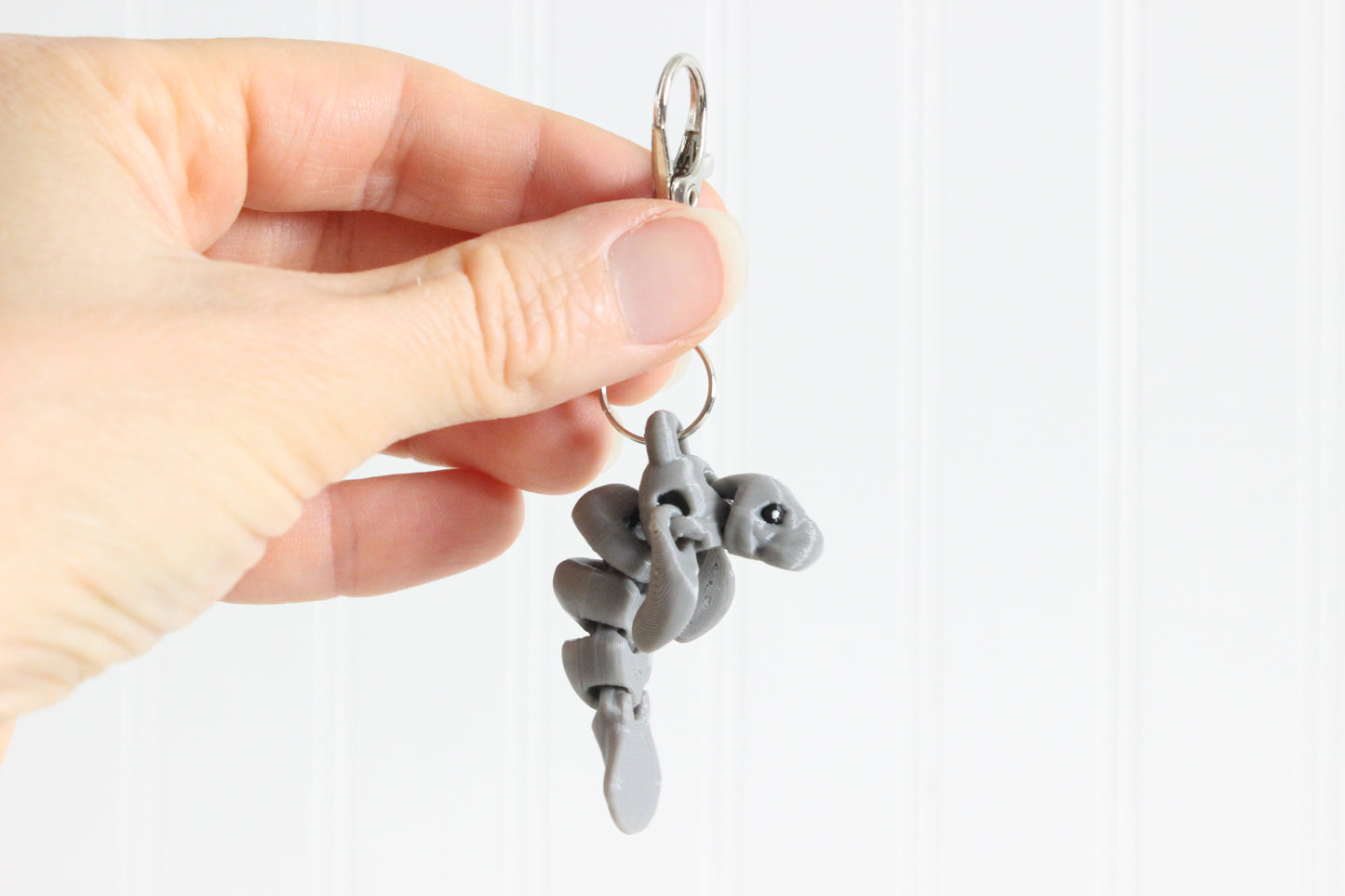 Hand holding the 3D-printed gray manatee keychain to show its size, colors, and silver swivel clip.