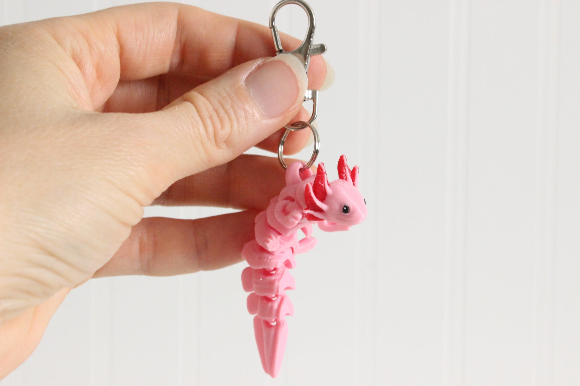 Hand holding a pink 3D-printed axolotl keychain to show its size and external gills.